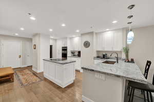 Kitchen featuring double oven, hanging light fixtures, sink, white cabinets, and light hardwood / wood-style floors