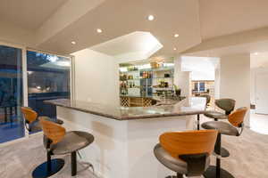 Bar featuring light carpet and dark stone counters