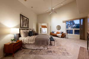 Carpeted bedroom featuring track lighting, high vaulted ceiling, and ceiling fan