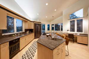 Kitchen featuring light brown cabinets, decorative light fixtures, black appliances, and vaulted ceiling