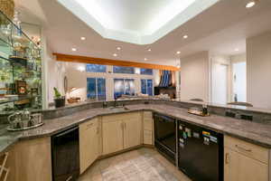 Kitchen with dark stone countertops, black dishwasher, sink, and kitchen peninsula