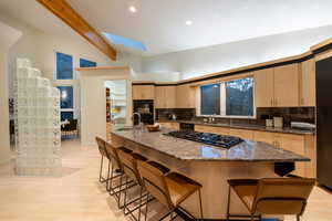 Kitchen with backsplash, vaulted ceiling with skylight, sink, and light wood-type flooring