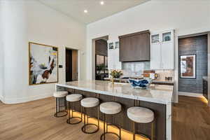 Kitchen with white cabinetry, sink, light stone counters, a center island with sink, and light wood-type flooring