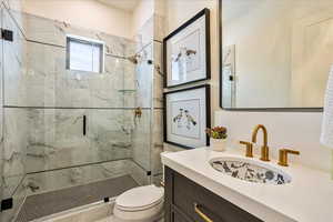 Bathroom featuring a shower with door, vanity, and toilet