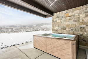 Snow covered patio featuring a mountain view, a hot tub, and ceiling fan