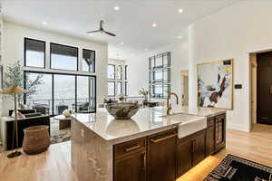 Kitchen featuring light stone countertops, sink, light hardwood / wood-style floors, a kitchen island with sink, and ceiling fan with notable chandelier