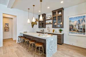 Bar featuring pendant lighting, light hardwood / wood-style floors, dark brown cabinetry, and light stone countertops