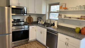 Kitchen with white cabinetry, sink, stainless steel appliances, dark stone countertops, and light hardwood / wood-style floors