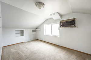 Additional living space featuring carpet floors, vaulted ceiling, and a wall mounted air conditioner