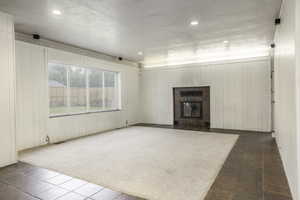 Unfurnished living room featuring wooden walls, a tiled fireplace, and dark colored carpet