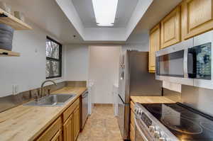 Kitchen featuring light brown cabinets, sink, a tray ceiling, appliances with stainless steel finishes, and butcher block counters