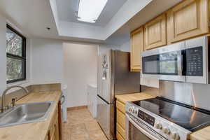 Kitchen with a raised ceiling, sink, stainless steel appliances, light brown cabinetry, and wood counters