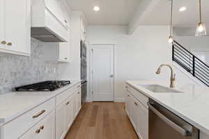 Kitchen with stainless steel appliances, sink, decorative light fixtures, light wood-type flooring, and premium range hood