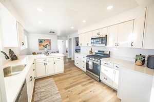 Kitchen with kitchen peninsula, appliances with stainless steel finishes, light wood-type flooring, sink, and white cabinets