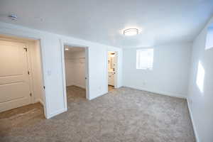 Unfurnished bedroom with connected bathroom, a spacious closet, a closet, and light colored carpet