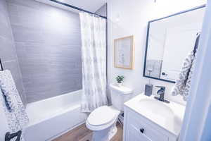 Full bathroom with hardwood / wood-style floors, vanity, toilet, and shower / bathtub combination with curtain