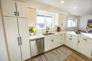 Kitchen featuring white cabinetry, dishwasher, sink, kitchen peninsula, and light hardwood / wood-style floors