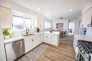 Kitchen with kitchen peninsula, appliances with stainless steel finishes, sink, light hardwood / wood-style flooring, and white cabinetry