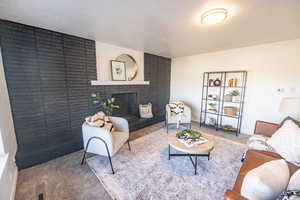 Living room featuring carpet, a textured ceiling, and a brick fireplace