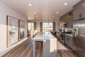 Kitchen with dark hardwood / wood-style floors, stainless steel appliances, a center island with sink, sink, and a breakfast bar