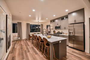 Kitchen featuring appliances with stainless steel finishes, a kitchen breakfast bar, decorative light fixtures, light hardwood / wood-style flooring, and a kitchen island with sink