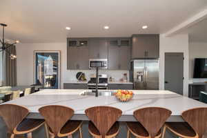 Kitchen featuring a kitchen breakfast bar, a notable chandelier, pendant lighting, appliances with stainless steel finishes, and tasteful backsplash