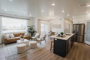 Kitchen with a center island with sink, stainless steel fridge with ice dispenser, white cabinetry, light hardwood / wood-style flooring, and sink