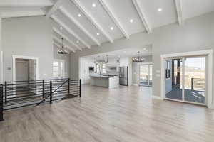 Living room with light waterproof laminate flooring, wrought iron staircase, and high vaulted beamed ceiling