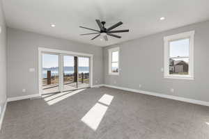 Carpeted primary room featuring a water and mountain view, sliding glass door, deck, and ceiling fan