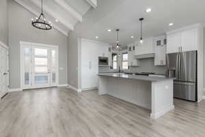 Kitchen with a center island, vaulted ceiling with beams, stainless steel appliances, and light waterproof laminate flooring