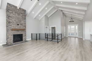 Unfurnished living room with waterproof laminate flooring, a stone fireplace, land high vaulted beamed ceiling