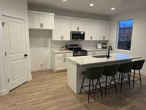 Kitchen featuring white cabinetry, light hardwood / wood-style flooring, an island with sink, and appliances with stainless steel finishes