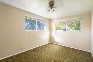 Carpeted empty bedroom with a healthy amount of sunlight and ceiling fan