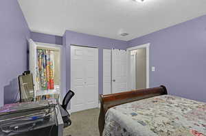 Bedroom featuring a textured ceiling, two closets, and light colored carpet