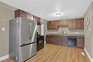 Kitchen with sink, black appliances, light stone counters, a textured ceiling, and light hardwood / wood-style floors