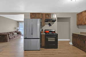 Kitchen featuring black gas stove, a textured ceiling, light hardwood / wood-style floors, and stainless steel refrigerator