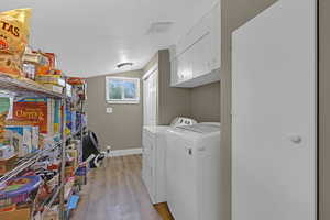 Washroom with washer and clothes dryer, a textured ceiling, light wood-type flooring, and cabinets