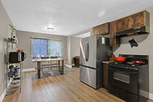 Kitchen featuring light wood-type flooring, dark brown cabinets, a textured ceiling, black gas range oven, and stainless steel refrigerator