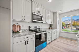 Kitchen featuring stainless steel appliances, light stone counters, light wood finished floors, a mountain view, and white cabinetry