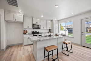 Kitchen featuring white cabinets, a kitchen bar, appliances with stainless steel finishes, light stone counters, and light wood-style flooring