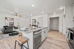 Kitchen featuring white cabinetry, light stone counters, a kitchen bar, light wood-style floors, and recessed lighting
