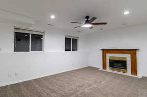 Unfurnished living room featuring ceiling fan, carpet floors, and a tile fireplace