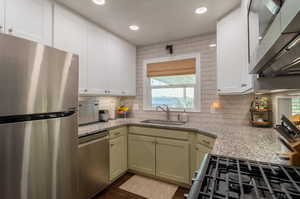 Kitchen featuring stainless steel appliances, sink, green cabinetry, light stone counters, and dark hardwood / wood-style flooring