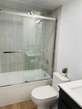 Full bathroom with shower / bath combination with glass door, vanity, wood-type flooring, and toilet