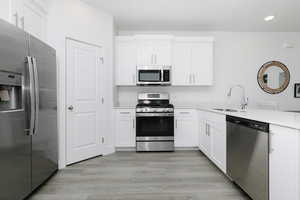 Kitchen featuring appliances with stainless steel finishes, white cabinets, sink, and light wood-type flooring