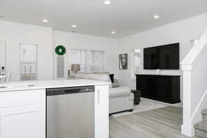 Kitchen with light hardwood / wood-style floors, sink, stainless steel dishwasher, and white cabinets