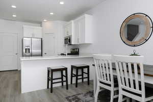 Kitchen with kitchen peninsula, white cabinets, a kitchen bar, light hardwood / wood-style flooring, and stainless steel appliances