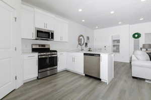 Kitchen featuring light hardwood / wood-style flooring, kitchen peninsula, white cabinets, and stainless steel appliances