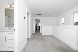 Corridor featuring sink and light colored carpet