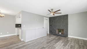 Unfurnished living room featuring a fireplace, ceiling fan with notable chandelier, and light wood-type flooring